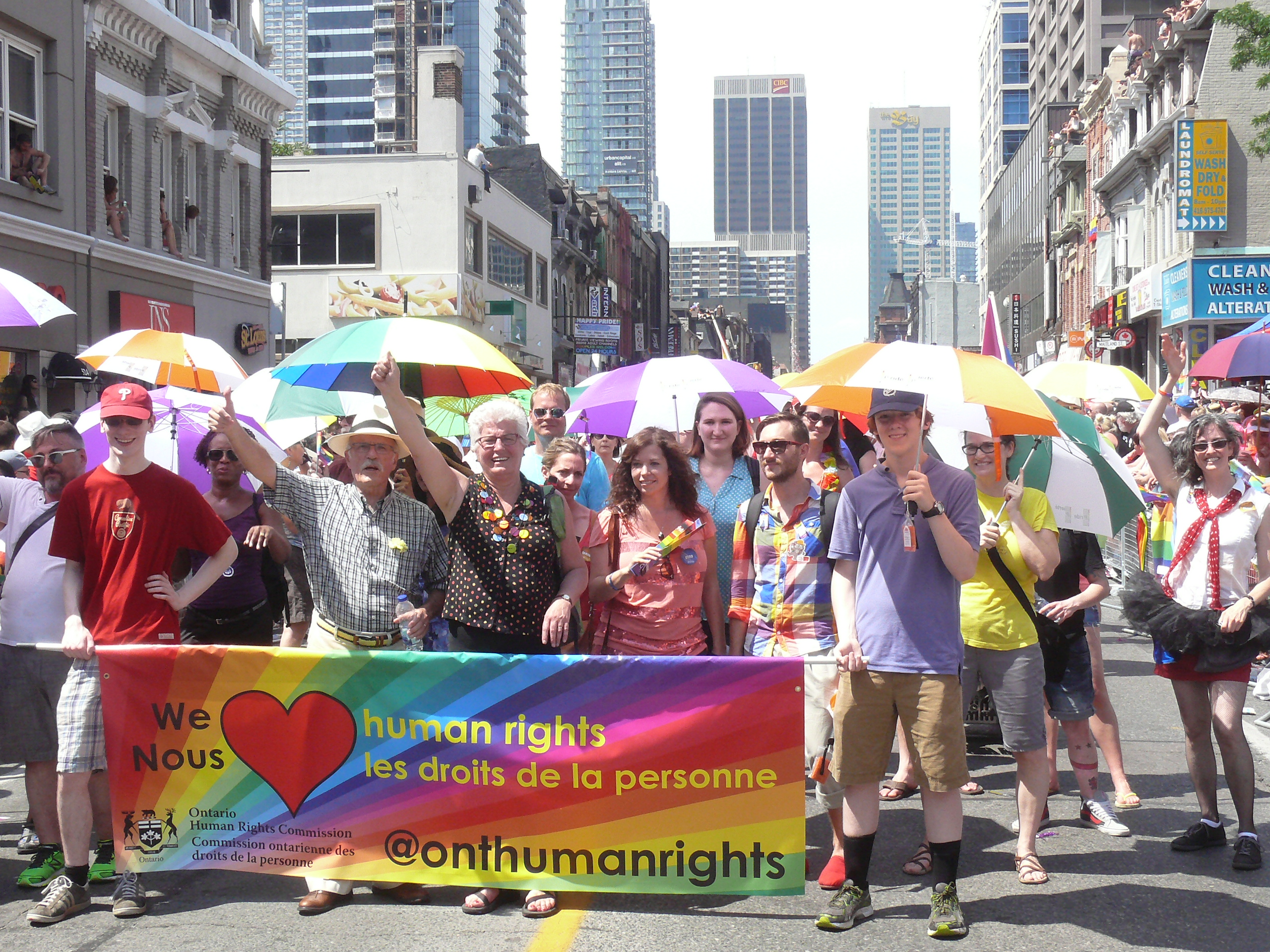 Chief Commissioner Barbara Hall, her husband Max, OHRC staff, family and friends march behind a large, colourful OHRC banner that says “We heart human rights” at the Pride parade.