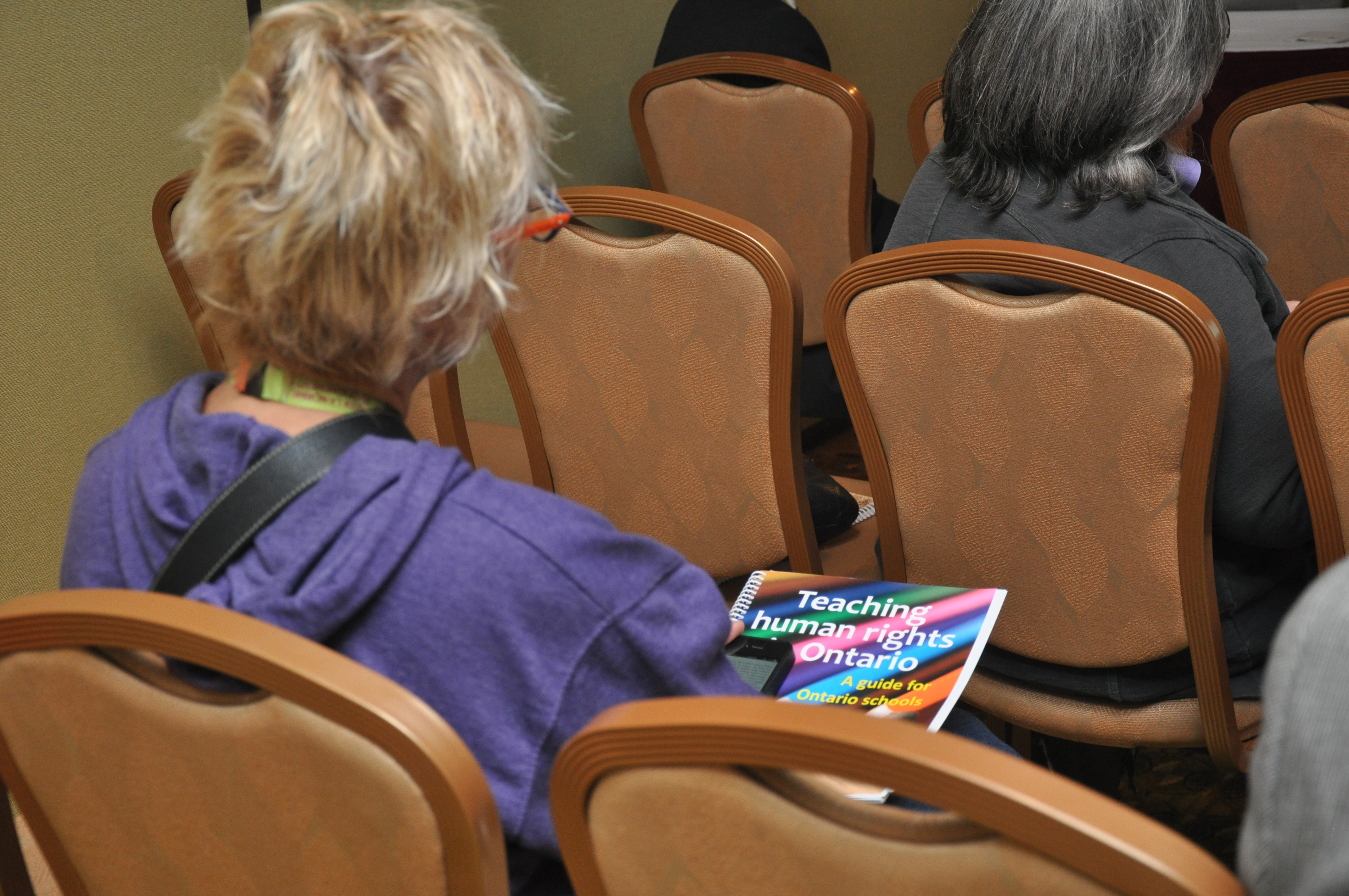 A woman holding a copy of Teaching human rights in Ontario sits in a chair.